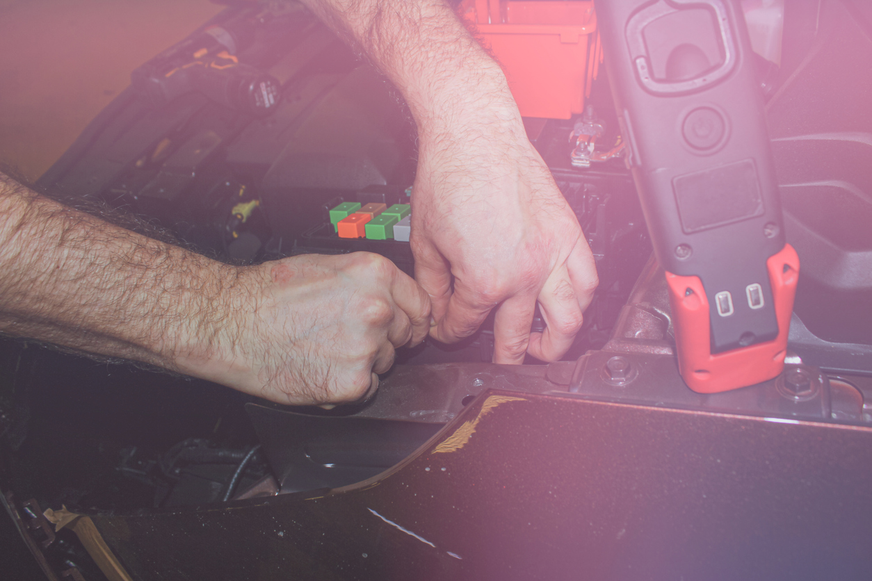 The concept of car service, repair, tuning, maintenance. The car electrician fixes problems in the electronics of the car. Hands of an electrician working with an electrical unit in a car close-up.